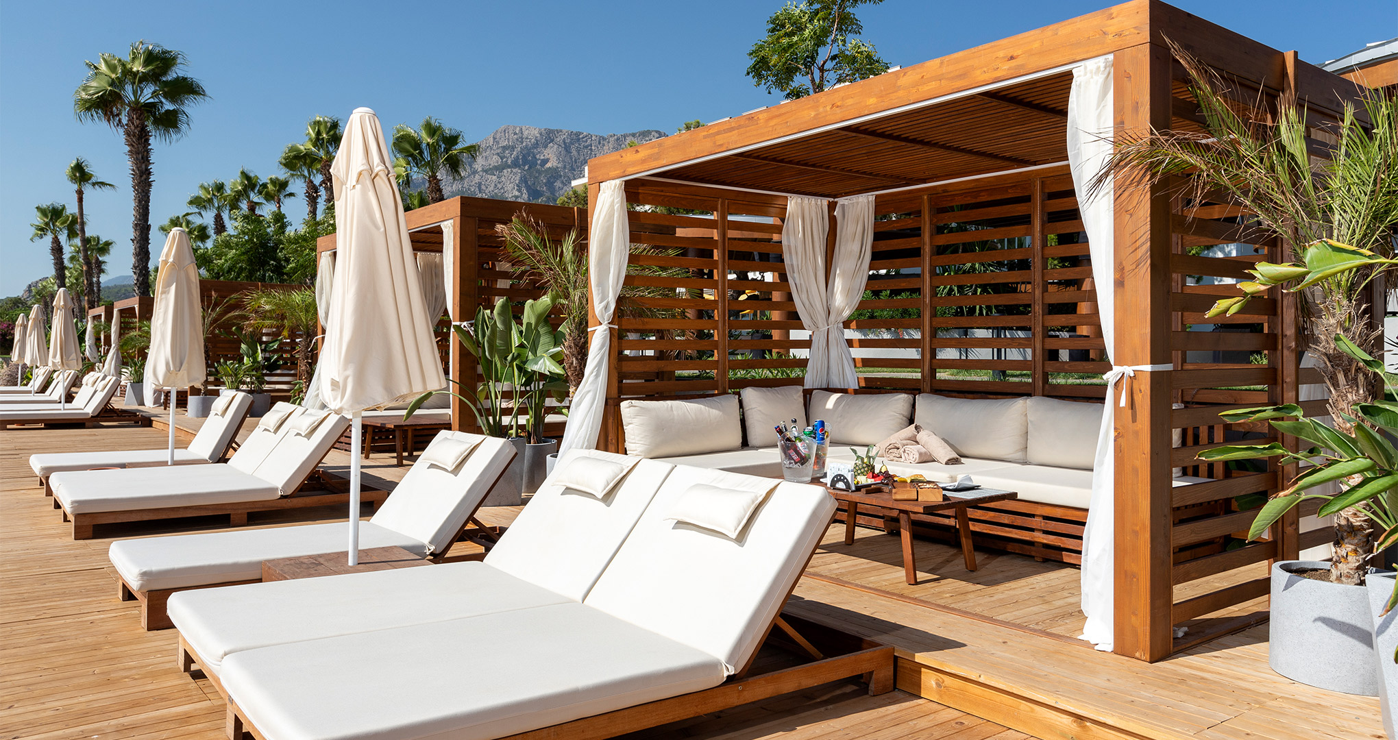 Plaża Sherwood Exclusive Kemer z leżakami, drewnianymi pawilonami i górami Beydağları